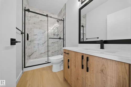Contemporary bathroom featuring a light wood-finish vanity with matte black hardware, a white integrated sink, and a black-framed mirror - 3285 Chernowski Way, Edmonton, AB - Indoor Photo Showing Bathroom