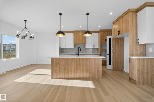Open-concept kitchen and dining area featuring light wood-finish flooring, a kitchen island with a built-in sink and matte black faucet, and a two-tone cabinetry scheme with light wood-finish and white upper cabinets - 3285 Chernowski Way, Edmonton, AB - Indoor Photo Showing Kitchen
