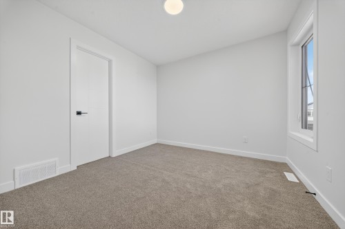 Bright interior space featuring light-colored carpeting, white walls, a white interior door with black hardware, and a window providing natural illumination - 3285 Chernowski Way, Edmonton, AB - Indoor Photo Showing Other Room