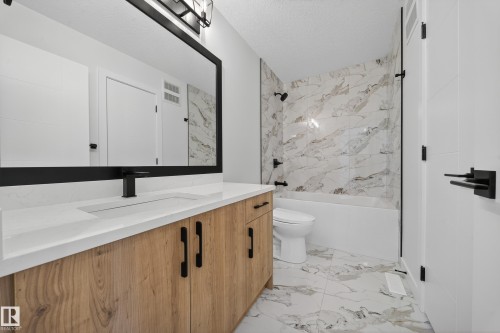 Bathroom featuring a wood-finish vanity with a built-in sink, a long mirror with a black frame, and a bathtub with tile surround - 3285 Chernowski Way, Edmonton, AB - Indoor Photo Showing Bathroom