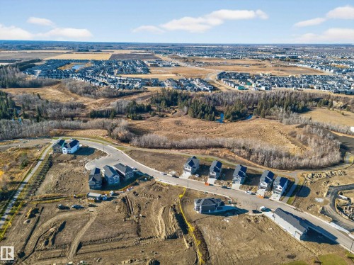 Aerial view of a developing residential area featuring new construction, existing homes, paved roadways, and surrounding natural landscapes with mature trees - 3285 Chernowski Way, Edmonton, AB - Outdoor With View
