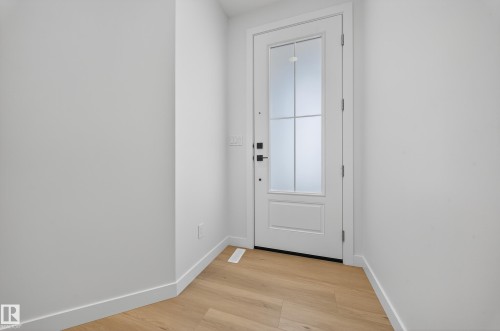 Entryway with light wood-finish flooring, white baseboards, and a white paneled door featuring frosted glass inserts and dark hardware - 3285 Chernowski Way, Edmonton, AB - Indoor Photo Showing Other Room