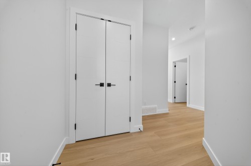 Bright white hallway featuring contemporary bifold doors with black hardware, wood-finish flooring, recessed lighting, and crisp white baseboards - 3285 Chernowski Way, Edmonton, AB - Indoor Photo Showing Other Room
