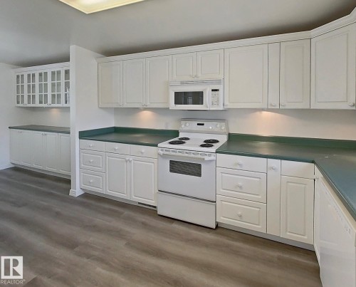 Functional kitchen featuring extensive white cabinetry with under-cabinet lighting, a built-in microwave, white electric range, and wood-finish flooring - 9624 75 Street, Edmonton, AB - Indoor Photo Showing Kitchen