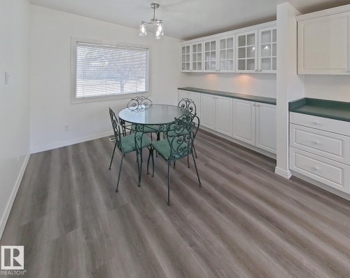 Spacious dining area featuring wood-finish flooring, a large window with blinds, and white built-in cabinetry with glass-front uppers and a dark countertop - 9624 75 Street, Edmonton, AB - Indoor Photo Showing Dining Room