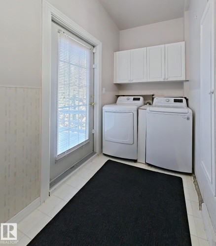 Laundry area featuring a full-light exterior door with integrated blinds, white tile flooring, and overhead cabinetry - 9624 75 Street, Edmonton, AB - Indoor Photo Showing Laundry Room