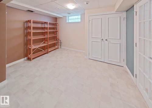 Spacious room featuring light-colored tile flooring, white baseboards, and a dropped ceiling with recessed lighting - 9624 75 Street, Edmonton, AB - Indoor