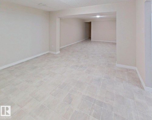 Spacious room featuring light-toned tiled flooring, neutral wall paint, and white baseboards - 9624 75 Street, Edmonton, AB - Indoor Photo Showing Other Room