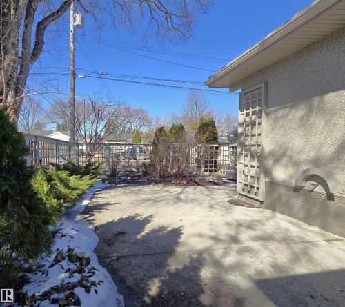 Concrete patio area featuring a textured stucco exterior, decorative wall trellis, and perimeter fencing - 9624 75 Street, Edmonton, AB - Outdoor