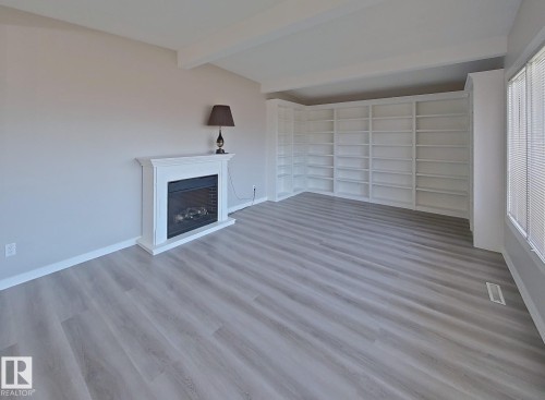 Living space featuring a white mantel fireplace, extensive built-in shelving, wood-finish flooring, and natural light from horizontal blinds - 9624 75 Street, Edmonton, AB - Indoor Photo Showing Other Room With Fireplace
