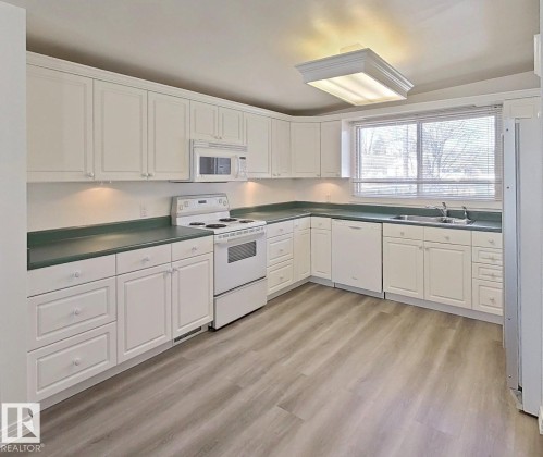 Kitchen featuring white cabinetry, dark green countertops, a white electric range, a built-in microwave, and wood-finish flooring - 9624 75 Street, Edmonton, AB - Indoor Photo Showing Kitchen With Double Sink
