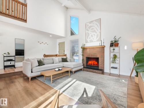 Living area featuring high vaulted ceilings, a brick fireplace, and light-toned flooring - 12219 25 Avenue, Edmonton, AB - Indoor Photo Showing Living Room With Fireplace