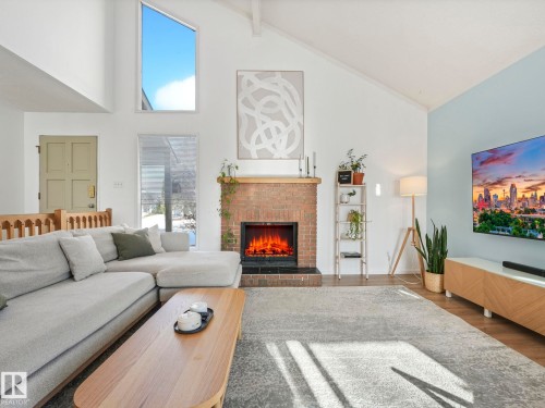 Living room featuring high vaulted ceilings, a brick fireplace, and large windows providing natural light - 12219 25 Avenue, Edmonton, AB - Indoor Photo Showing Living Room With Fireplace