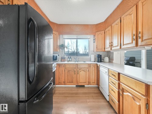 The kitchen features wood cabinetry, a window above the sink, and a black refrigerator - 12219 25 Avenue, Edmonton, AB - Indoor Photo Showing Kitchen