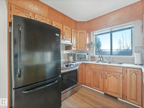 The kitchen features light wood cabinetry, a double basin stainless steel sink, and light-colored countertops - 12219 25 Avenue, Edmonton, AB - Indoor Photo Showing Kitchen With Double Sink