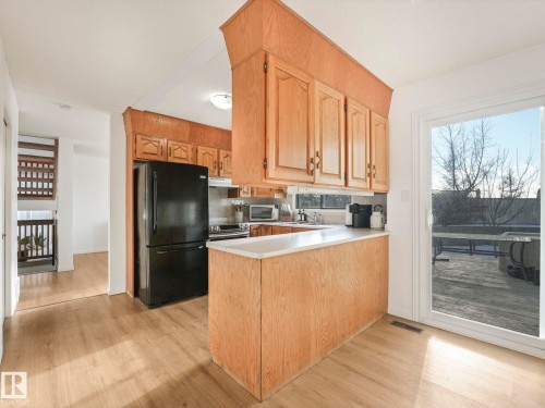 The kitchen features light wood cabinetry, a black refrigerator, and an oven - 12219 25 Avenue, Edmonton, AB - Indoor Photo Showing Kitchen
