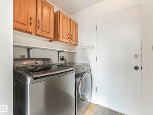 Laundry area featuring a top-load washing machine, a front-load dryer, wood cabinetry, and a white door - 12219 25 Avenue, Edmonton, AB - Indoor Photo Showing Laundry Room
