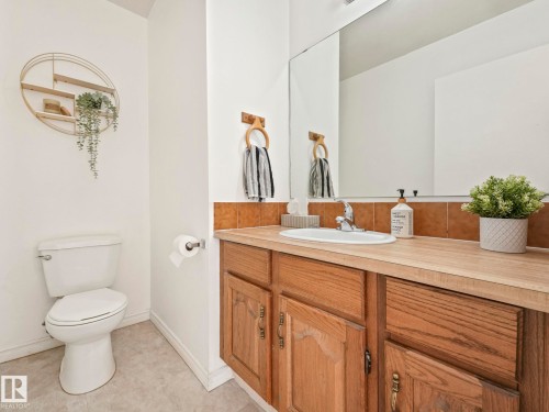 The bathroom features a vanity with a light wood countertop, a built-in sink, and a mirror - 12219 25 Avenue, Edmonton, AB - Indoor Photo Showing Bathroom