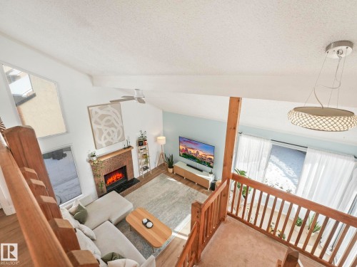 Spacious living area featuring a brick fireplace, tall windows, and exposed wooden beams - 12219 25 Avenue, Edmonton, AB - Indoor With Fireplace