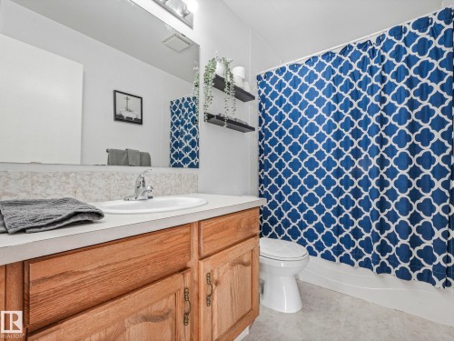 The bathroom features a vanity with a light-colored countertop and wood cabinetry, a mirror, and a toilet - 12219 25 Avenue, Edmonton, AB - Indoor Photo Showing Bathroom