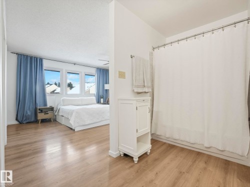 The property features neutral-toned flooring throughout, with a bedroom area showcasing large windows and blue curtains - 12219 25 Avenue, Edmonton, AB - Indoor Photo Showing Bedroom