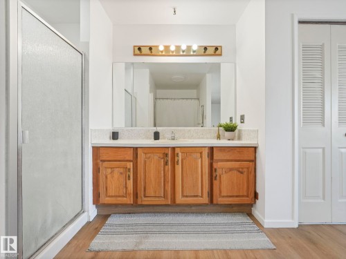 This bathroom features a shower with a translucent glass door, a vanity with a light-colored countertop and a mirror, and wood-paneled cabinets - 12219 25 Avenue, Edmonton, AB - Indoor Photo Showing Bathroom