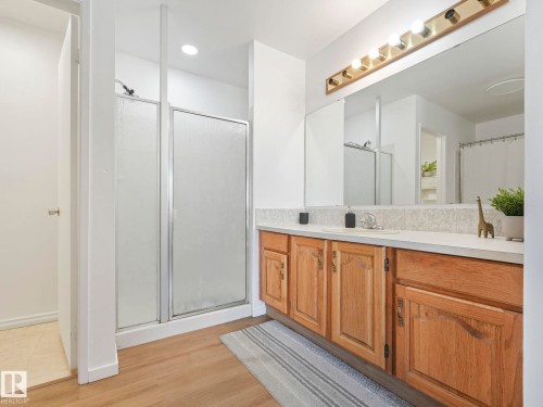 Bathroom featuring a shower with a clear and frosted glass enclosure, a vanity with wood cabinetry, a light-colored countertop, and a large mirror - 12219 25 Avenue, Edmonton, AB - Indoor Photo Showing Bathroom