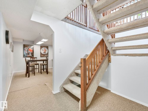 The property features carpeted flooring throughout, with a well-maintained staircase featuring wooden banisters - 12219 25 Avenue, Edmonton, AB - Indoor Photo Showing Other Room