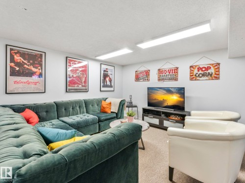 Living area featuring a large sectional sofa, two armchairs, a television on a media console, and overhead lighting - 12219 25 Avenue, Edmonton, AB - Indoor