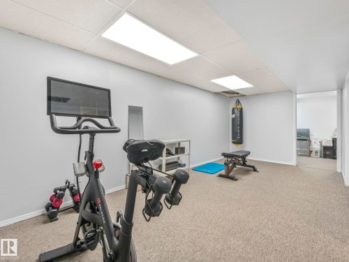 The property features a dedicated fitness area with carpeted flooring and light grey walls - 12219 25 Avenue, Edmonton, AB - Indoor Photo Showing Gym Room