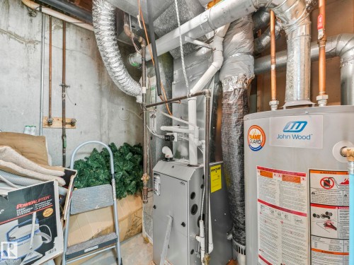 The property features a water heater and furnace with exposed ductwork, set against concrete walls - 12219 25 Avenue, Edmonton, AB - Indoor Photo Showing Basement