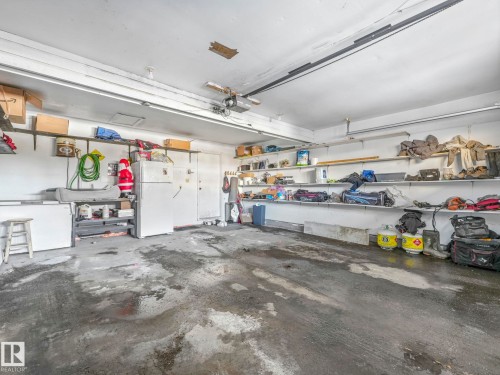The property features a garage with a concrete floor, built-in shelving, and a garage door track system - 12219 25 Avenue, Edmonton, AB - Indoor Photo Showing Garage