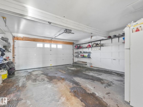 The garage features a white panel door with windows, concrete flooring, and overhead shelving for storage - 12219 25 Avenue, Edmonton, AB - Indoor Photo Showing Garage