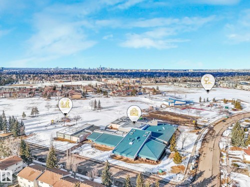 The property is situated within a community featuring residential buildings, a school with a blue roof, and open fields - 12219 25 Avenue, Edmonton, AB - Outdoor With View