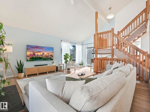 The living area features a vaulted ceiling, light wood-style flooring, and large windows providing natural light - 12219 25 Avenue, Edmonton, AB - Indoor Photo Showing Living Room