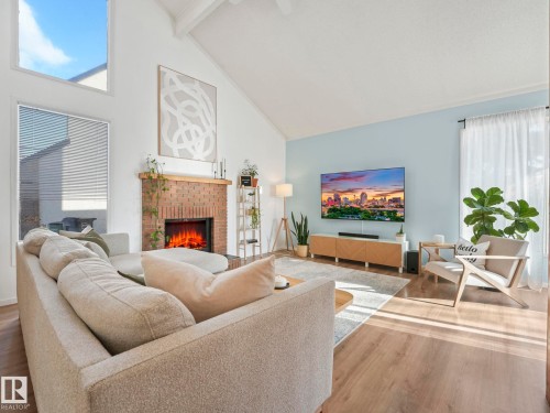 This living area features a vaulted ceiling, a brick fireplace, and warm-toned flooring - 12219 25 Avenue, Edmonton, AB - Indoor Photo Showing Living Room With Fireplace