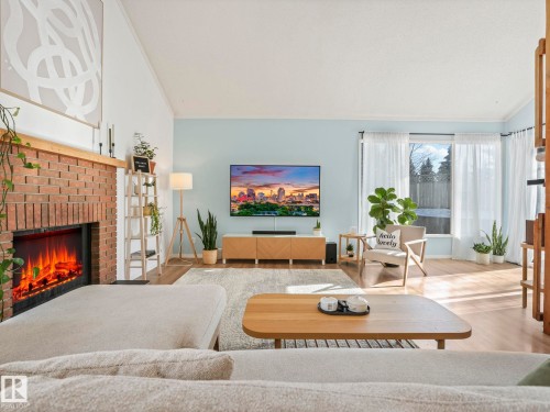 The living room features vaulted ceilings, a brick fireplace with a wood mantle, and light wood flooring - 12219 25 Avenue, Edmonton, AB - Indoor Photo Showing Living Room With Fireplace