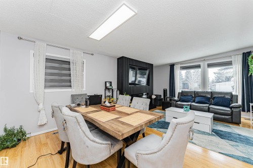 This open concept living space features hardwood flooring, a dining area with a wooden table, and a living area with large windows - 10412 39 Avenue, Edmonton, AB - Indoor Photo Showing Other Room