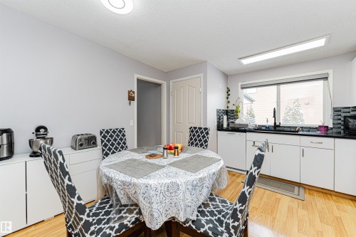 The kitchen features light wood flooring, white cabinetry, a black countertop, and a black tile backsplash - 10412 39 Avenue, Edmonton, AB - Indoor Photo Showing Dining Room