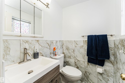 Bathroom with a modern vanity, white sink, and stone tile wainscoting - 10412 39 Avenue, Edmonton, AB - Indoor Photo Showing Bathroom