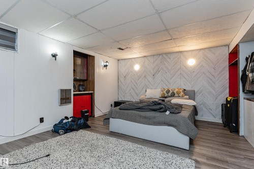 This room features wood-look flooring, a white paneled ceiling, and a decorative accent wall with a chevron pattern - 10412 39 Avenue, Edmonton, AB - Indoor Photo Showing Bedroom