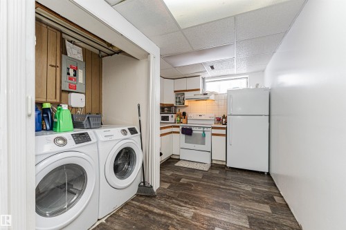 The property features a dedicated laundry area with white front-loading machines, and a kitchen area with white cabinetry, a window, and a white refrigerator - 10412 39 Avenue, Edmonton, AB - Indoor Photo Showing Laundry Room