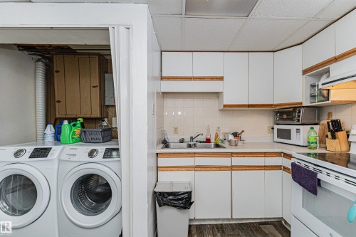 The kitchen features white cabinetry with wood trim, a double basin stainless steel sink, and a white tiled backsplash - 10412 39 Avenue, Edmonton, AB - Indoor Photo Showing Laundry Room