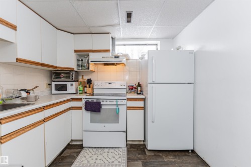 The kitchen features white cabinetry with wood trim, a white tile backsplash, and a white refrigerator - 10412 39 Avenue, Edmonton, AB - Indoor Photo Showing Kitchen