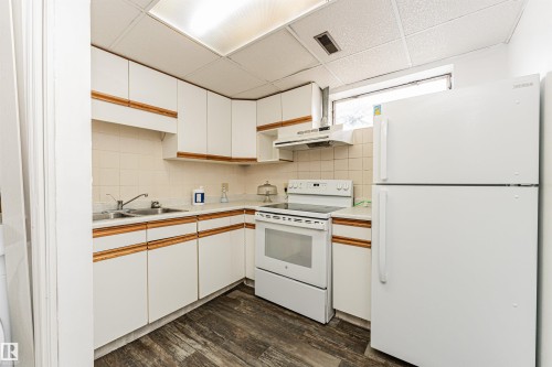 Kitchen featuring white cabinetry with wood-finish accents, a double basin stainless steel sink, a white electric range, a white refrigerator, and wood-finish flooring - 10412 39 Avenue, Edmonton, AB - Indoor Photo Showing Kitchen With Double Sink