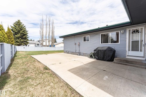 Rear exterior featuring light grey siding, a white storm door, and an expansive concrete patio - 10412 39 Avenue, Edmonton, AB - Outdoor