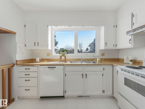 Kitchen featuring white cabinetry, light wood-toned countertops, a white dishwasher, and a window above the sink - 3421 112A Street, Edmonton, AB - Indoor Photo Showing Kitchen With Double Sink