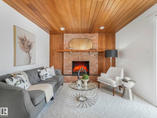 Living room featuring a wood-paneled ceiling, a brick fireplace with a mantel, and light-colored carpeting - 3421 112A Street, Edmonton, AB - Indoor Photo Showing Living Room With Fireplace