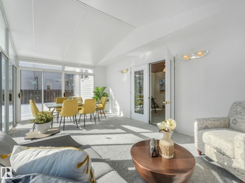 Bright sunroom featuring a pitched roof, light-colored carpeting, sliding glass doors, and a set of white French doors - 3421 112A Street, Edmonton, AB - Indoor Photo Showing Living Room