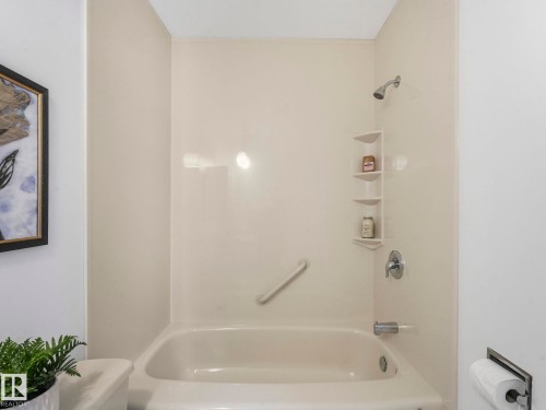 Bathroom featuring a bathtub with an integrated shower, built-in shelving, and a grab bar - 3421 112A Street, Edmonton, AB - Indoor Photo Showing Bathroom
